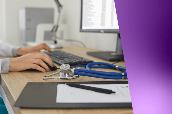 Doctor using electronic health record (EHR) software on a desktop computer, with stethoscope and patient chart on desk—illustrating digital medical documentation in clinical settings.